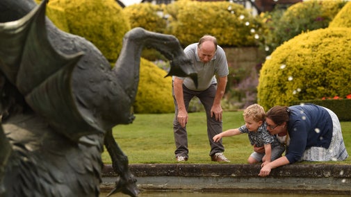 Family by the low stone edge of the Venus Fountain, with droplets of water falling and part of a dragon statue, at Ascott, Buckinghamshire
